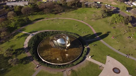 aerial tracking shot of flower steel sculpture and crowd of people relaxing in park while sunny day - buenos aires,capital of argentina