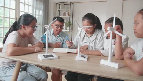 asian group of thoughtful kids study about ecology problems and their solution with wind turbine model and globe at school. renewable energy