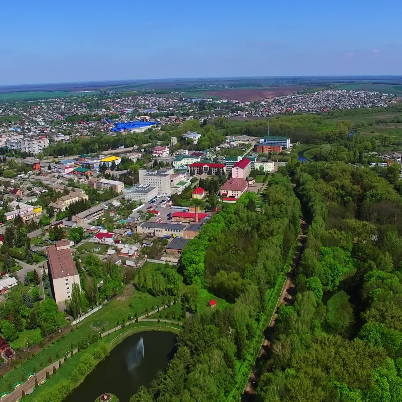 Cityscape with river and lots of trees on sunny day. Clear blue sky at backdrop. Aerial perspective