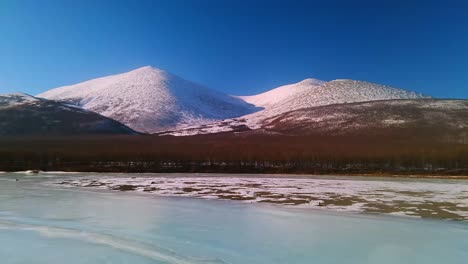 volando sobre un río congelado y un bosque gris en la soleada yakutia en un dron