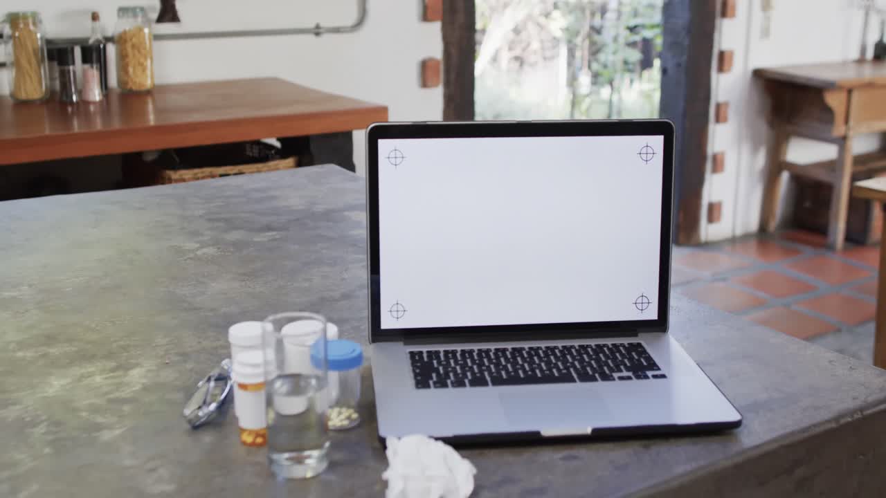 Close up of medication and laptop with copy space on screen on worktop in kitchen, slow motion