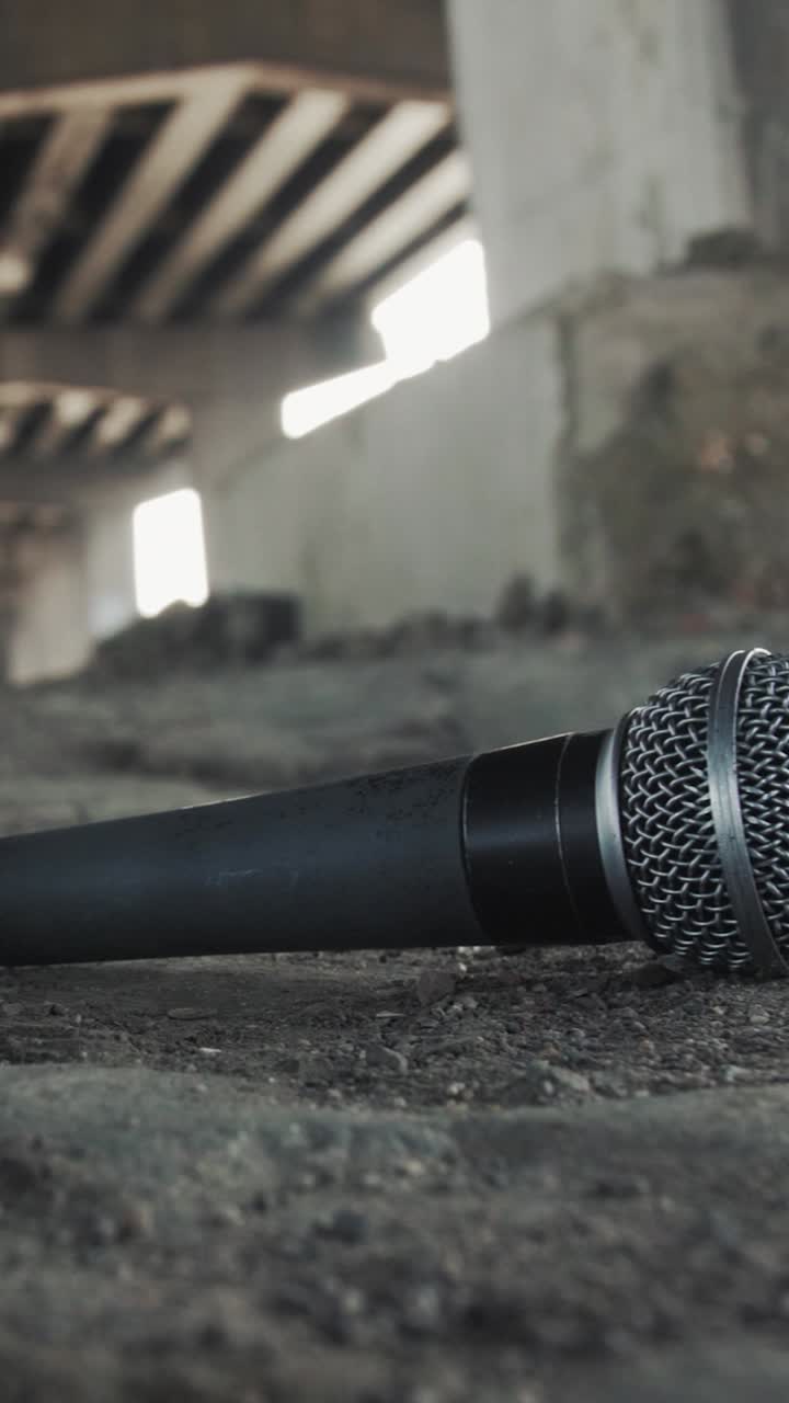 Smooth pan reveals dusty handheld mic and loose cable on gritty ground beneath a concrete highway overpass