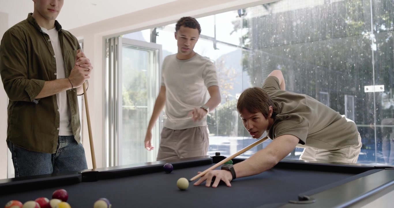 Diverse male friends gathering at pool table, one placing cue ball, one shooting for fun