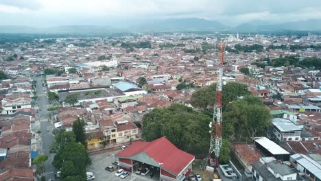 aerial-view-of-a-rural-town-in-Colombia,-with-clouds-hovering-above-the-mountains-in-the-background