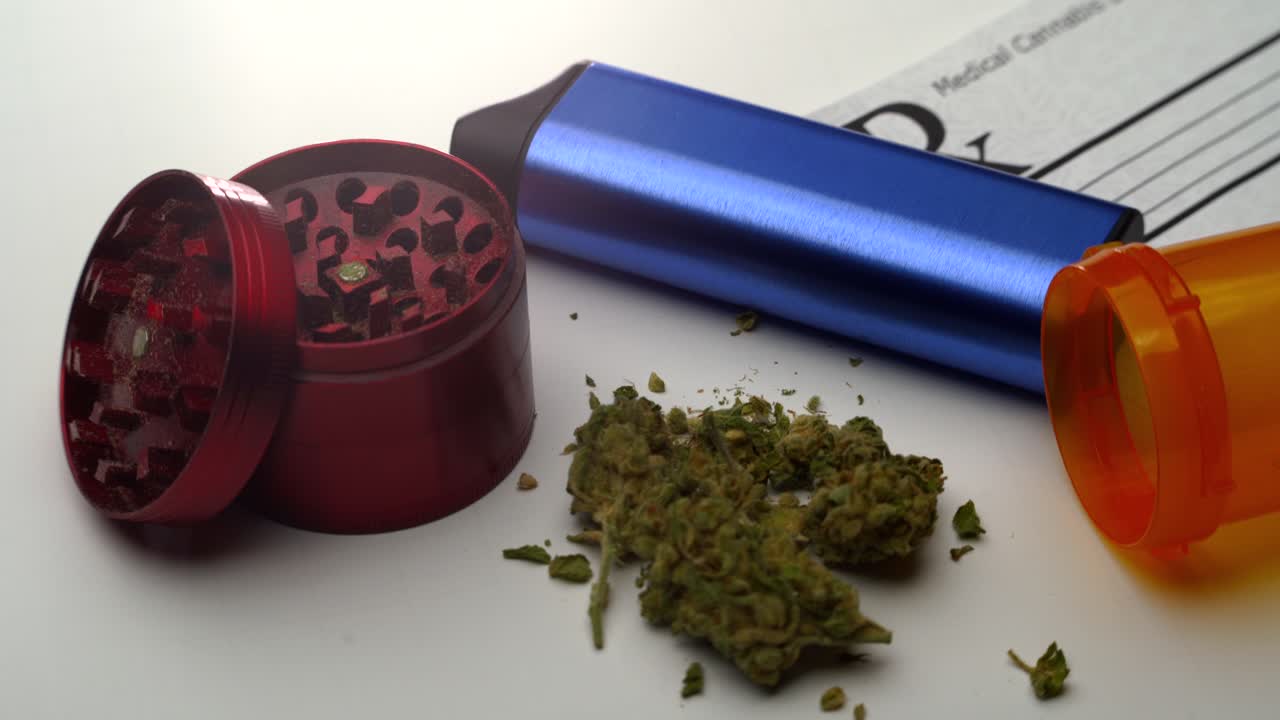 paneo muy lento a través de una nota de prescripción, vaporizador azul, molinillo rojo, frasco de pastillas abierto y una pequeña pila de marihuana en una mesa