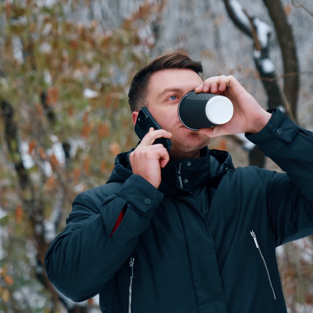 Uomo caucasico dai capelli scuri beve caffè e parla al telefono. Uomo a passeggio nel parco invernale.