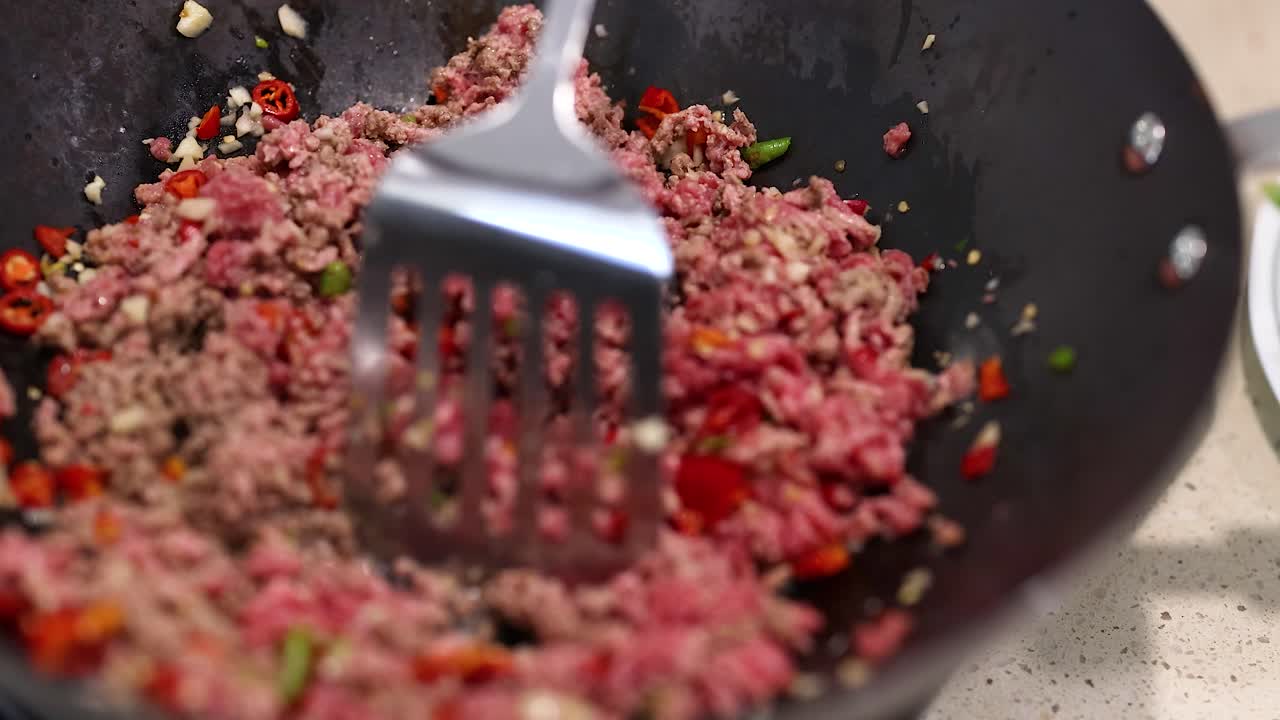 Beef and vegetables are stir-fried in a wok using a spatula. Bright lighting highlights the vibrant colors and textures