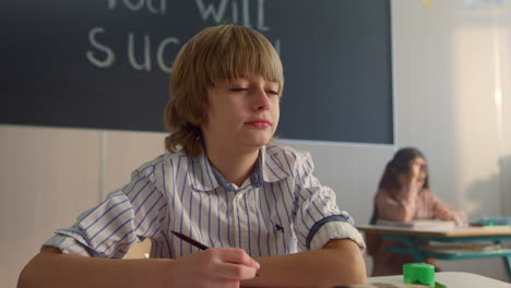 bored pupil sitting at desk in classroom. smart student writing in notebook