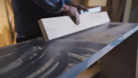 the carpenter is measuring the wood with a meter on his dusty workbench.