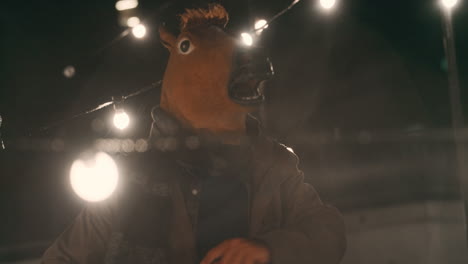 Un-Hombre-Gracioso-Con-Máscara-De-Caballo-Bailando-Bajo-La-Lluvia-En-La-Azotea-Divirtiéndose-Realizando-Movimientos-De-Baile-Tontos-Celebrando-El-Fin-De-Semana