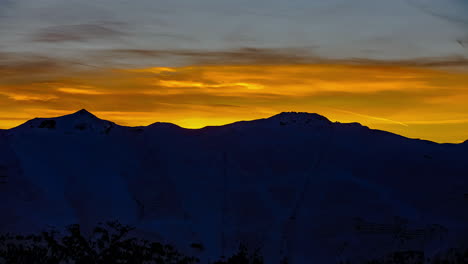 time lapse shot of sun coloring sky in orange and golden colors behind mountain range silhouette