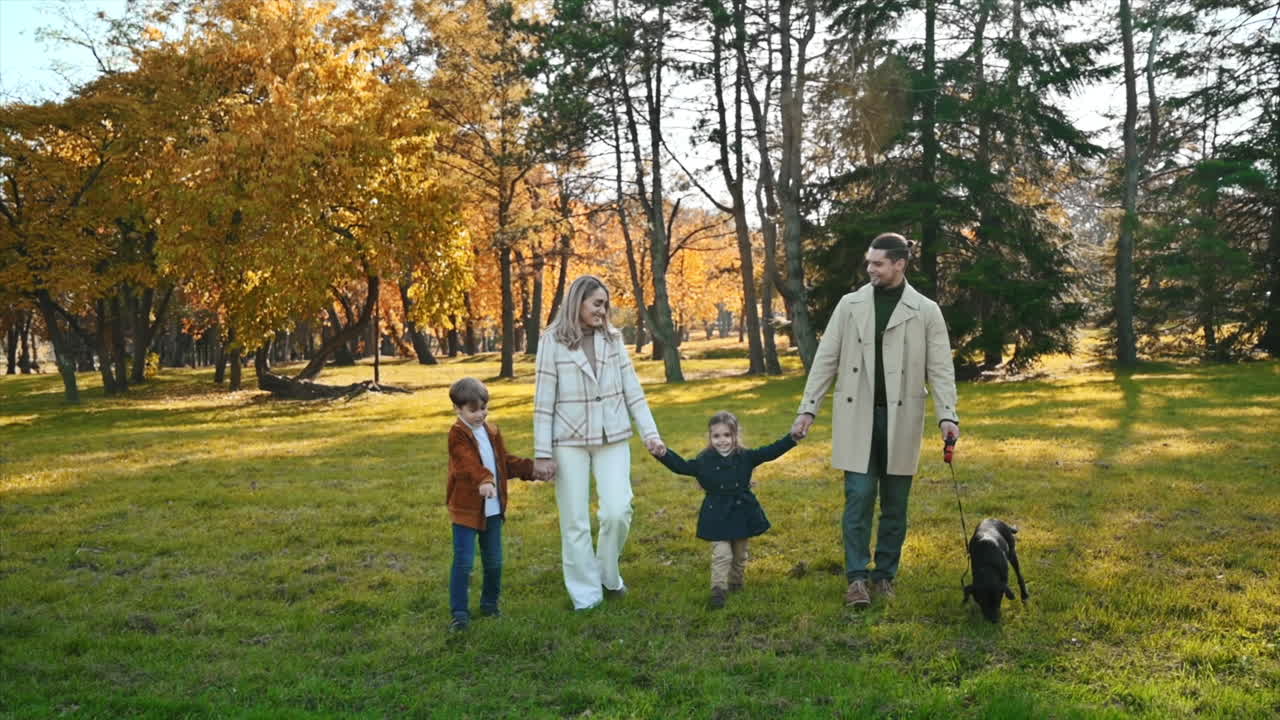 Happy family in an autumn park. Mother and father walking with daughter, son and their dog, yellowed trees around