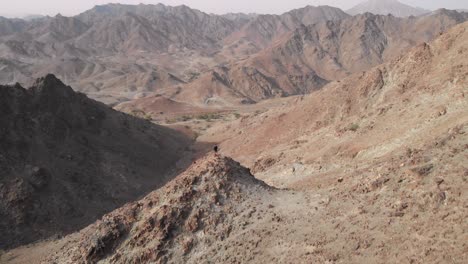 toma épica aérea de un dron de un joven parado en la cima de una montaña rocosa en hatta, emiratos árabes unidos