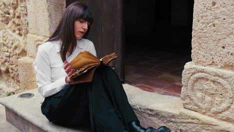 young woman reading an ancient book with passion sitting on a building steps
