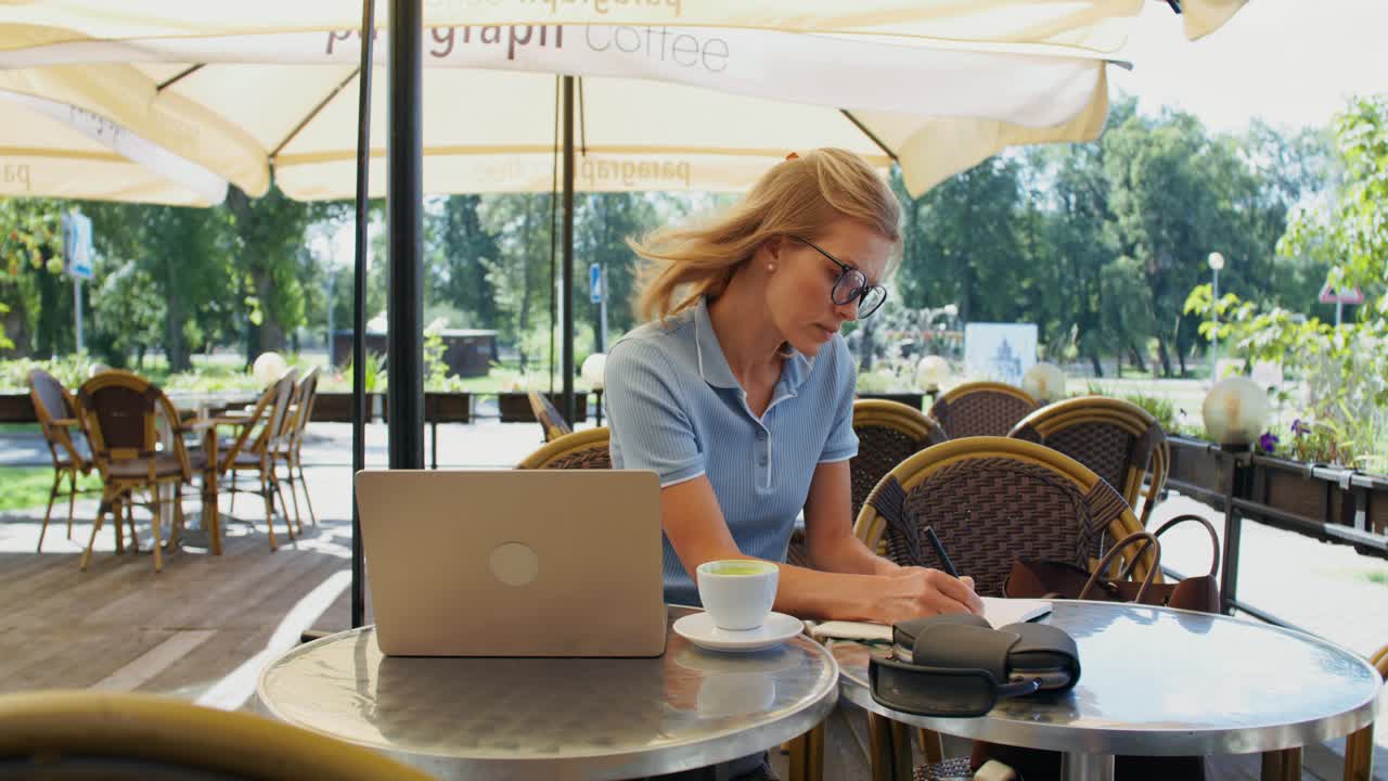 Frau arbeitet an einem Laptop in einem Café im Freien