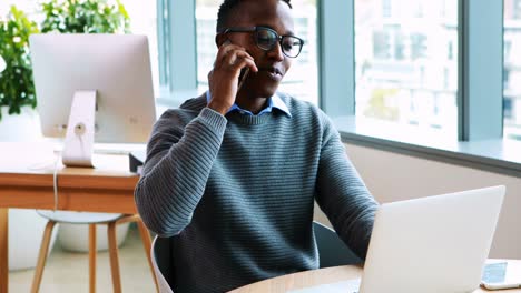 Male-executive-using-laptop-while-talking-on-mobile-phone