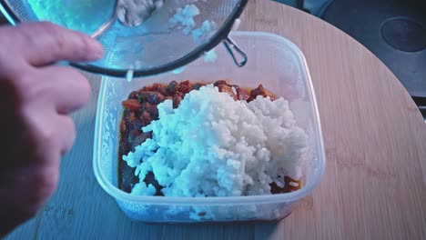 Adding-Rice-Into-Food-Container-Filled-With-Cooked-Spicy-Chicken-With-Beans