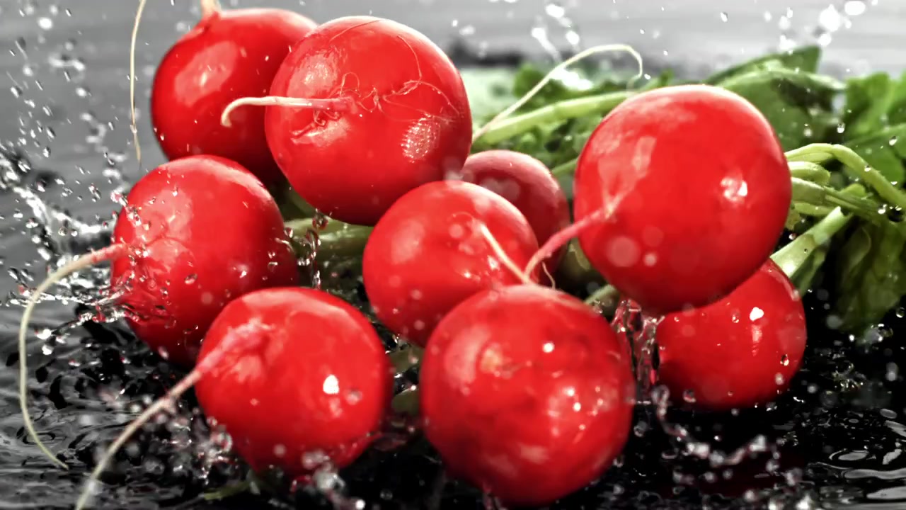 Frische rote Radieschen fallen in Zeitlupe ins Wasser