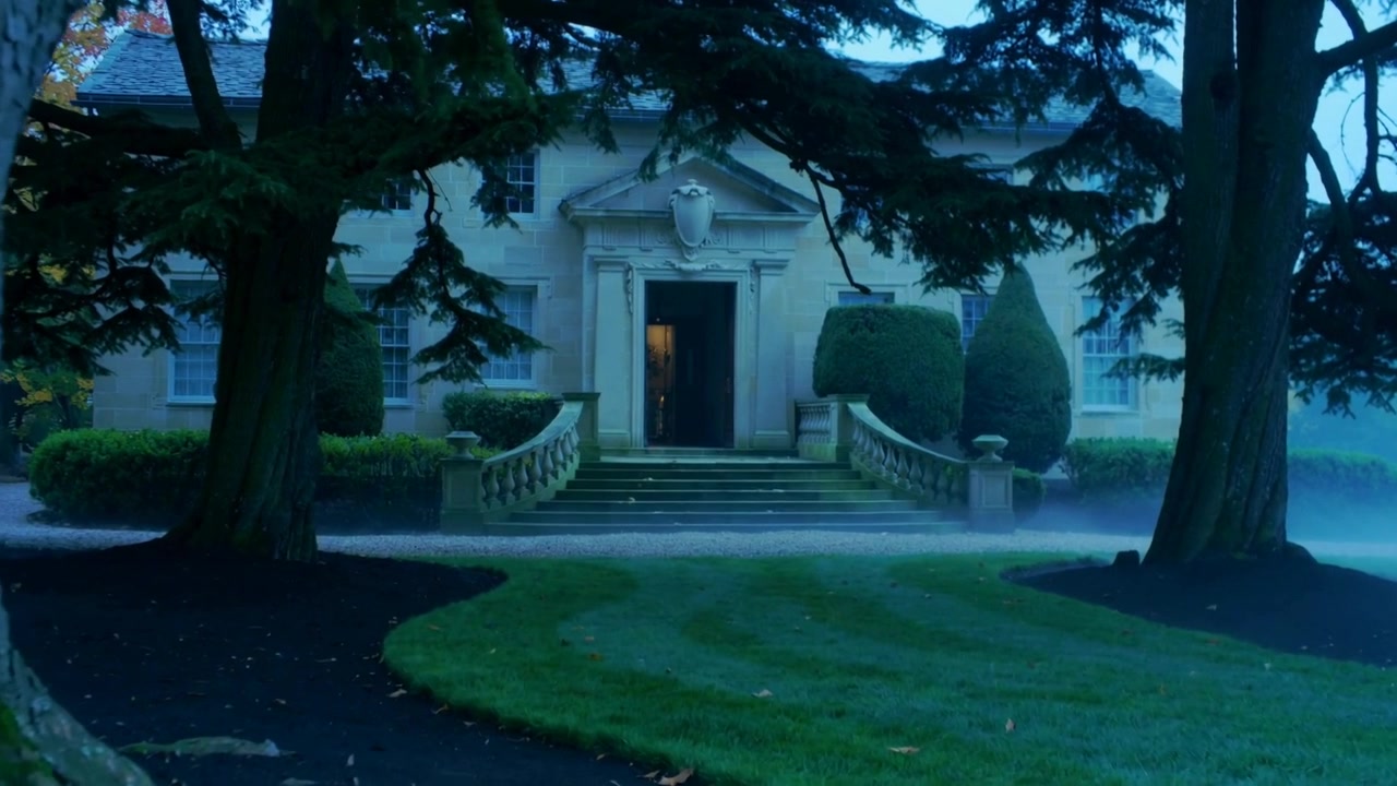 Stirring gentle breeze moving low fog toward stone mansion entrance at twilight, warm doorway light