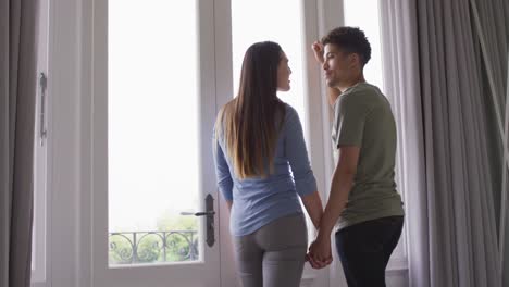 행복한 이중 인종 부부가 손을 잡고 창문을 통해 함께 바라보고 있습니다.