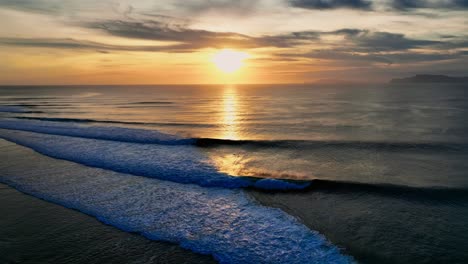 Drone-clip-showing-perfect-waves-breaking-at-bright-golden-sunset-in-Java,-Indonesia