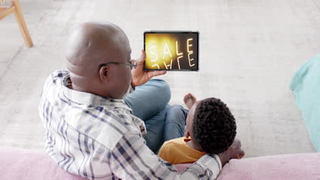 African-american-grandfather-and-grandson-using-tablet,-shopping-online-during-sale,-slow-motion