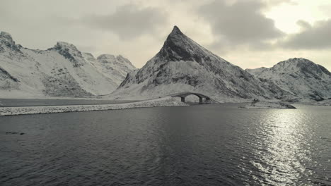 Drone-shot-of-a-bridge-near-mountains-in-winter