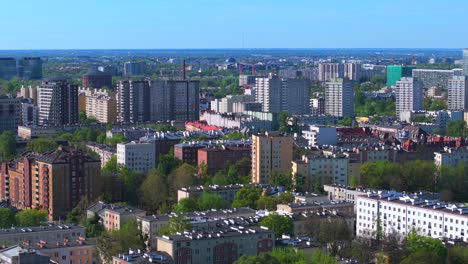 aerial establishing shot of warsaw’s wola district showing dense urban skyline, mid-rise apartments, and green pockets under a clear sky