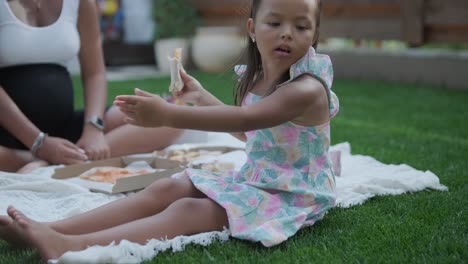 a mother and daughter enjoy a summer picnic outdoors on a grassy lawn, sharing pizza and spending quality time together on a sunny day. the family bonding scene reflects leisure and relaxation.