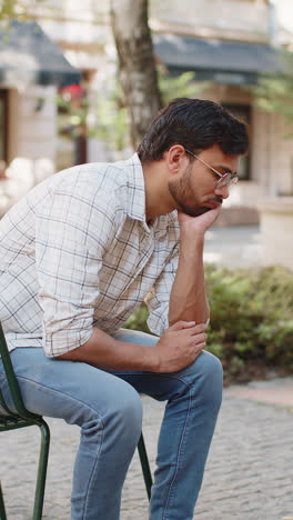 frustrated indian young man thinking of money debt budget loss bankruptcy sitting on chair on street