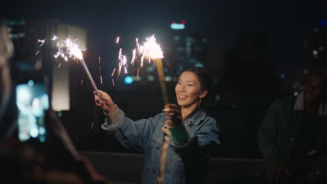 happy young asian woman holding sparklers dancing on rooftop at night celebrating new years eve enjoying holiday party celebration