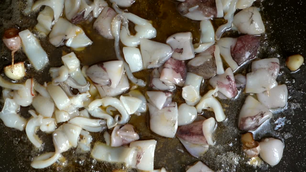 overhead view of cuttlefish with garlic on friendose paellon in olive oil in slow motion