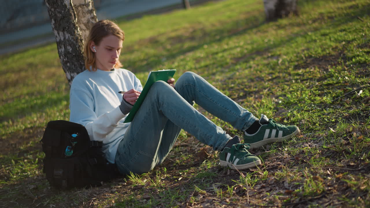 야외에서 공부하는 젊은이, 평화롭고 조용한 야외에서 차분하게 필기를 마무리하며 휴식을 취하는 젊은 학생, 고요한 환경에서 휴식을 취하며 야외에서 과제를 끝내는 젊은이