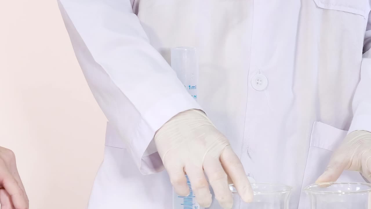 A scientist in a white coat carefully handles chemicals using glassware and a dropper in a laboratory setting.
