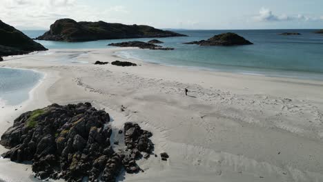 Walker-on-sandy-beach-on-Isle-of-Mull,-Scotland,-tracking-shot,-aerial