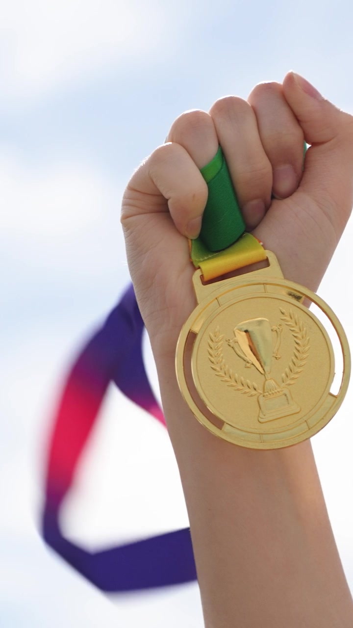Primer plano de una mano sosteniendo una medalla de oro con el cielo exterior de fondo. Concepto de logro, éxito, victoria, motivación, reconocimiento y realización personal
