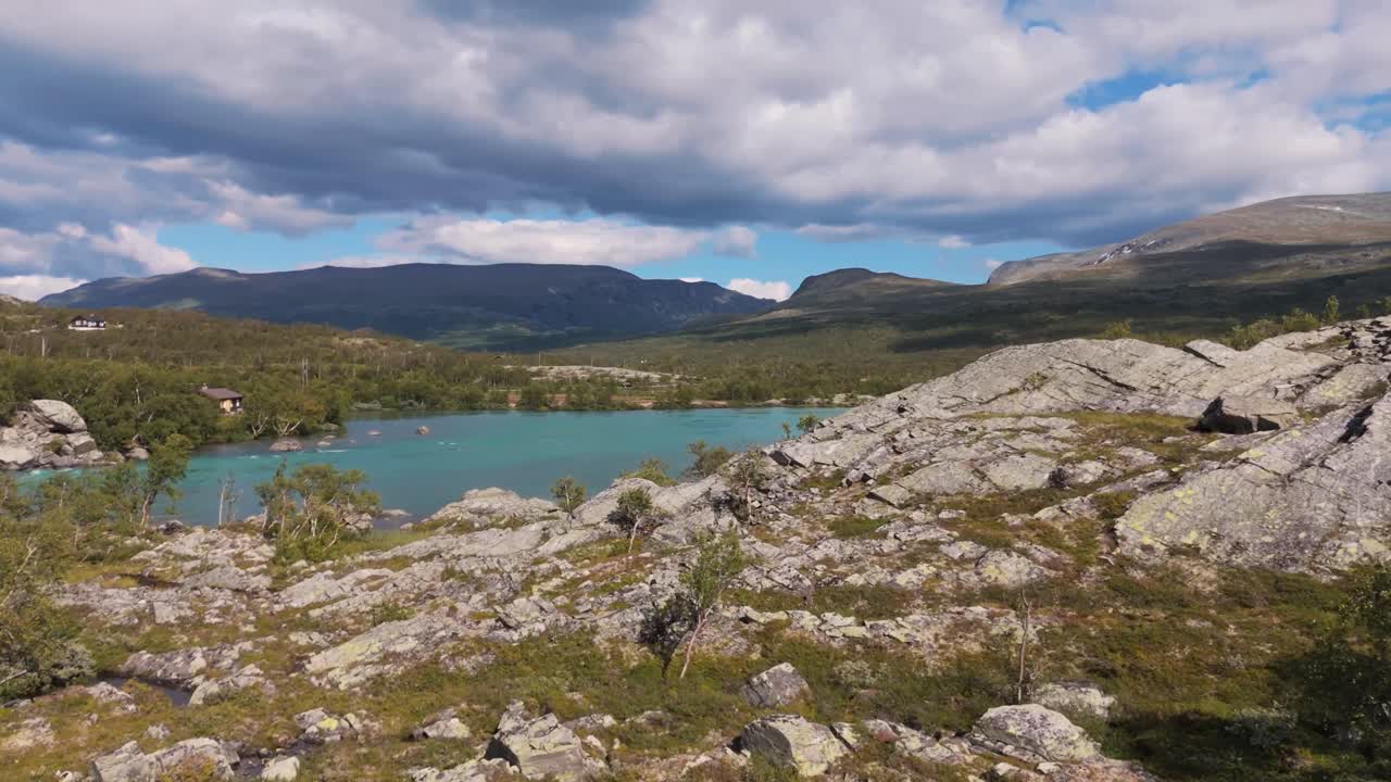 Aerial view of rocky wilderness in Norway with clear blue water, green trees, and mountains in the background under a cloudy sky