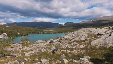 aerial view of rocky wilderness in norway with clear blue water, green trees, and mountains in the background under a cloudy sky