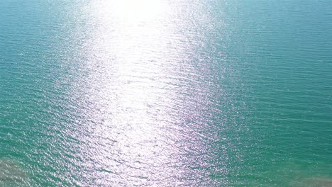 aerial view of sunlit turquoise water and cracked earth coastline