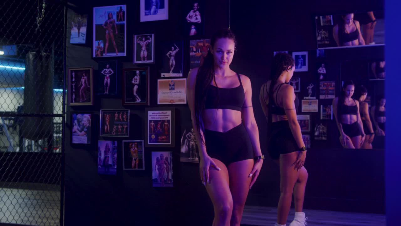 Fit girl posing in front of a mirror in gym while smiling at the camera