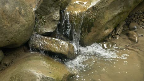 Cámara-Lenta-De-La-Corriente-De-Agua-Que-Fluye-Sobre-Rocas-Desgastadas-Por-El-Tiempo-En-El-Corazón-De-Un-Bosque