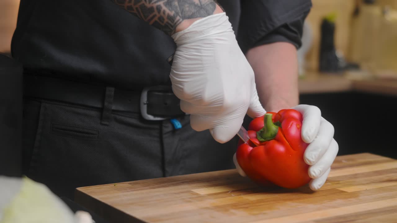 pimiento rojo fresco dividido en una tabla de madera por un joven chef profesional con un elegante pantalones negro con tatuajes
