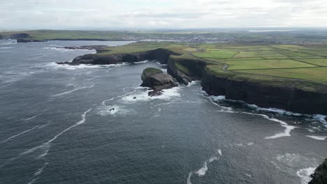 irish coastline with waves crashing against cliffs, green fields in the distance