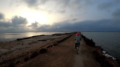 Biker-Frau,-Die-Bei-Sonnenuntergang-In-Zeitlupe-Fahrrad-Durch-Den-Strand-Fährt