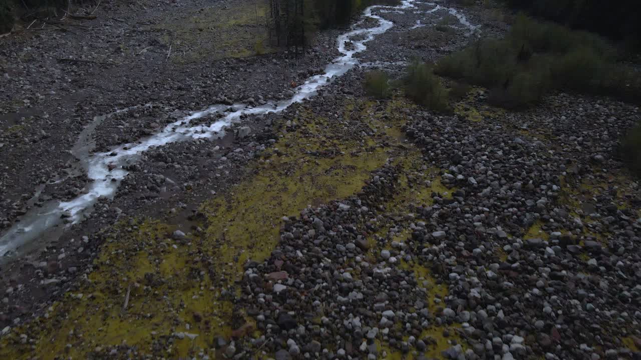 Aerial drone shot flying above a rocky creek at Mount Rainier with mountains rising in the background