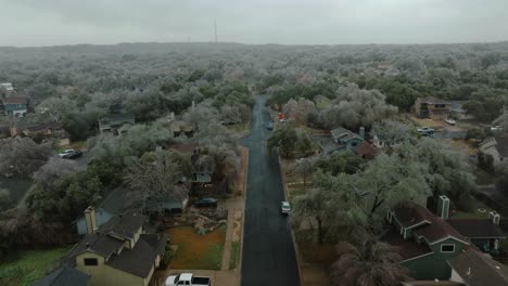 frozen icy trees in austin texas suburban neighborhood during cold winter freeze, aerial flyover street and tilt up over oak hill homes