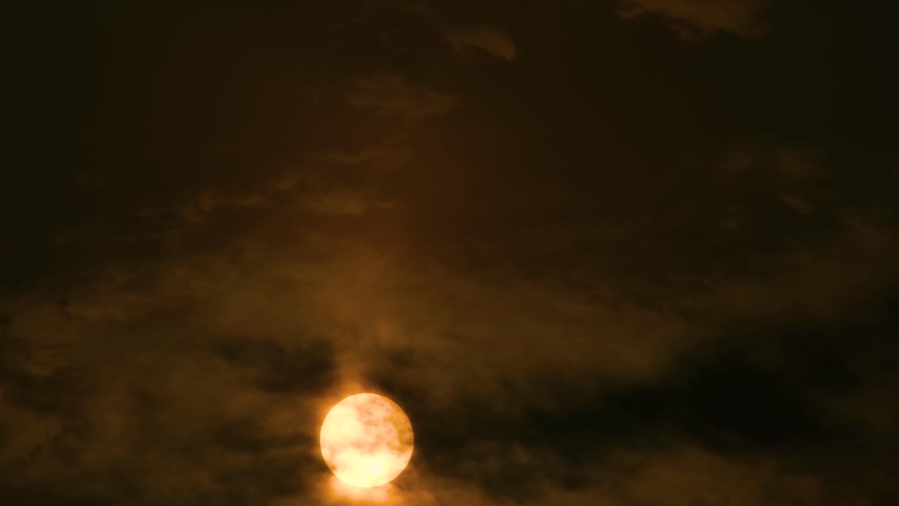 Gylden sol skinner, mens mørke skyer bevæger sig hen over en mørk himmel