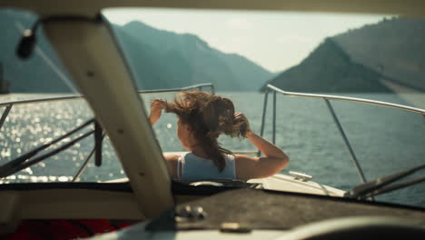 positive female sits on motorboat deck at windy seaside in sunny weather. young woman sails yacht in ocean on exotic vacation. tourist area viewing