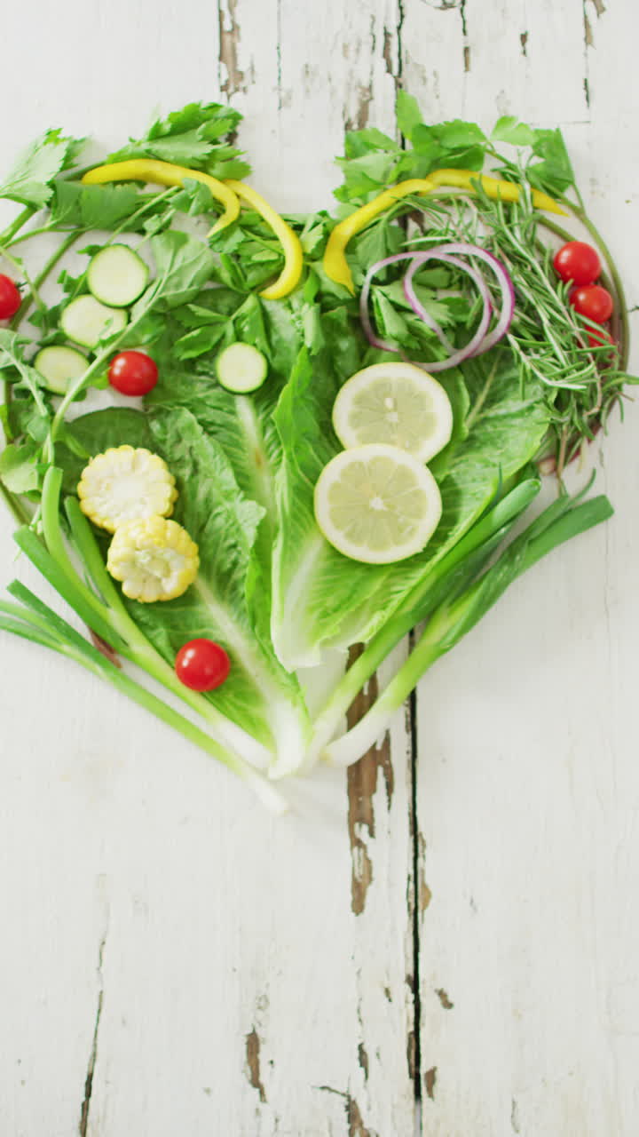 video vertical de tomates frescos y verduras verdes que forman un corazón sobre un fondo rústico blanco