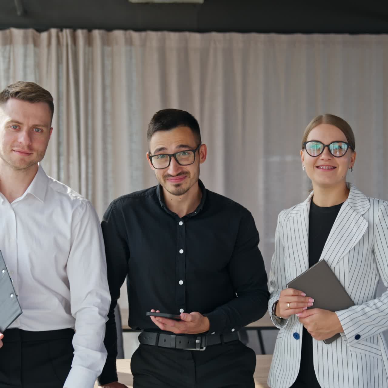Brunet man in glasses holding phone at his ear. Male and female colleagues standing beside him with papers in their hands
